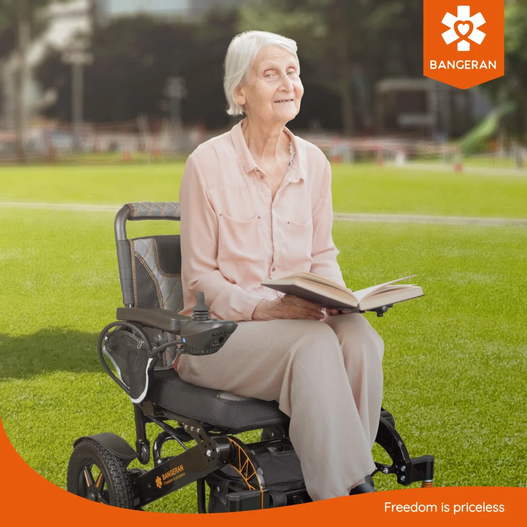Live image of elderly woman sitting on Bangeran Mammoth wheelchair reading a book in the park.